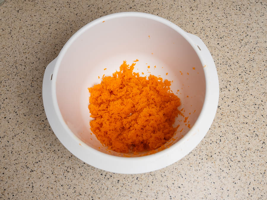 Finomra reszelt sárgarépa egy fehér műanyag tálban, növényi alapú húshelyettesítő recept előkészítése közben.