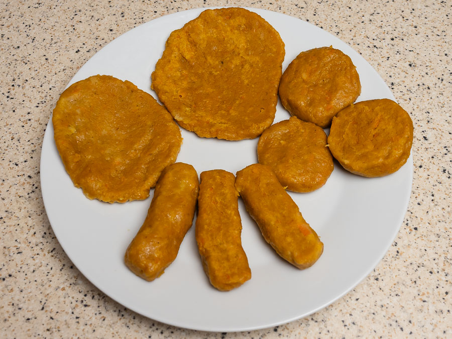 Párolt vegán csicseriborsó szeletek, kolbászkák és fasírtok fehér tányéron tálalva – növényi alapú húshelyettesítő recept részeként.
