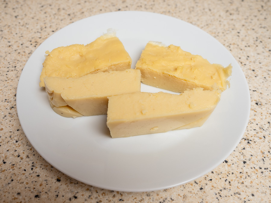 Szeletelt, világos színű házi csicseriborsó tofu egy fehér tányéron, világos munkalapon.