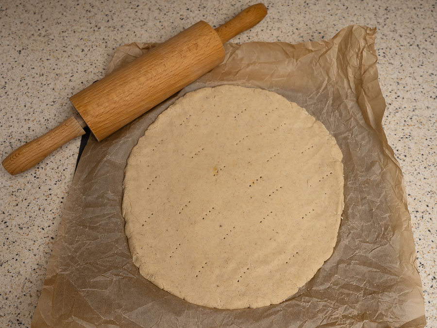 Gluténmentes pizza nyers tésztája kinyújtva sütőpapíron, villával megszurkálva