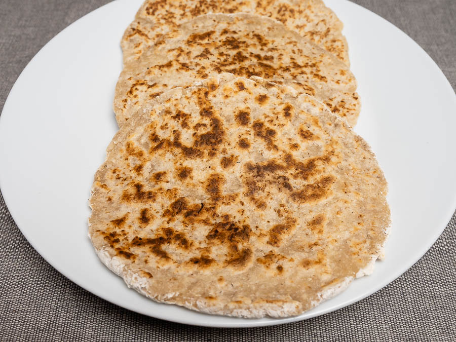 Négy frissen sült házi pita kenyér közeli nézetben, pöttyösre pirult felülettel fehér tányéron