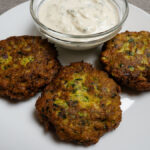 Három aranybarnára sült görög cukkini fasírt krémes vegán tzatzikivel fehér tányéron tálalva